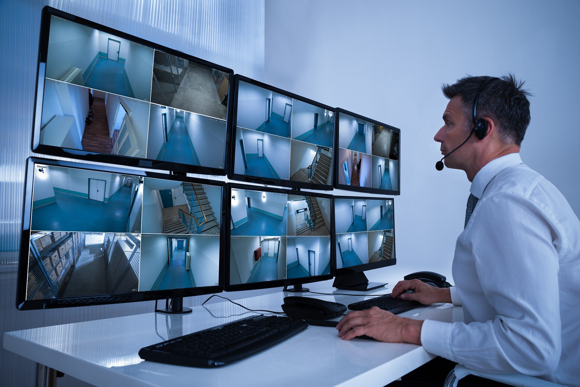 Man looking through security videos on six screens